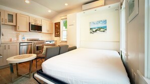 A compact room with a bed, kitchenette, and a painting of a beach scene. - Cozy Cape Cod Cottage in  Provincetown (Provincetown)