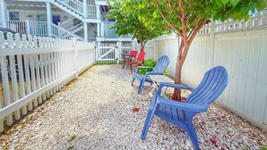 A multi-story building with a white exterior, a white picket fence, and a gravel patio with Adirondack chairs. - Cozy Cape Cod Cottage in  Provincetown (Provincetown)