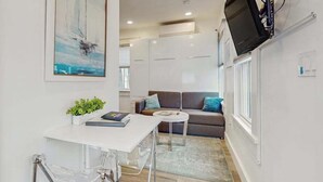 A compact living space with a white desk, a sofa, a small round table, and a mounted TV. - Cozy Cape Cod Cottage in  Provincetown (Provincetown)