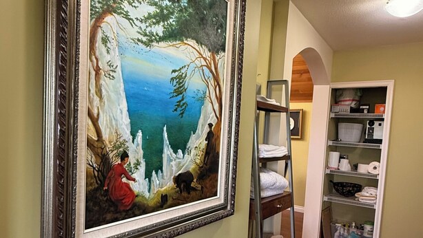 Un couloir avec un tableau encadré, un plancher en bois et une étagère blanche.