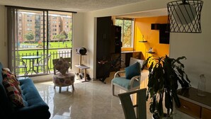 A spacious living area with a large sliding glass door leading to a balcony, a sofa, a chair, a small table, and a potted plant. - Cozy, family and pet-friendly apartment, located right beside a beautiful park. (Bogotá)