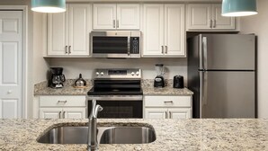A modern kitchen with white cabinets, stainless steel appliances, granite countertops, and pendant lighting. - 2 bedroom near Disney with pools and golf courses on the property. (Kissimmee)
