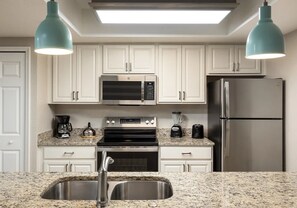Una cocina moderna con armarios blancos, electrodomésticos de acero inoxidable, encimeras de granito e iluminación colgante.