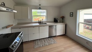 Eine moderne Küche mit Einbauherd, weißen Schränken, einem großen Fenster und einer Kaffeemaschine.
