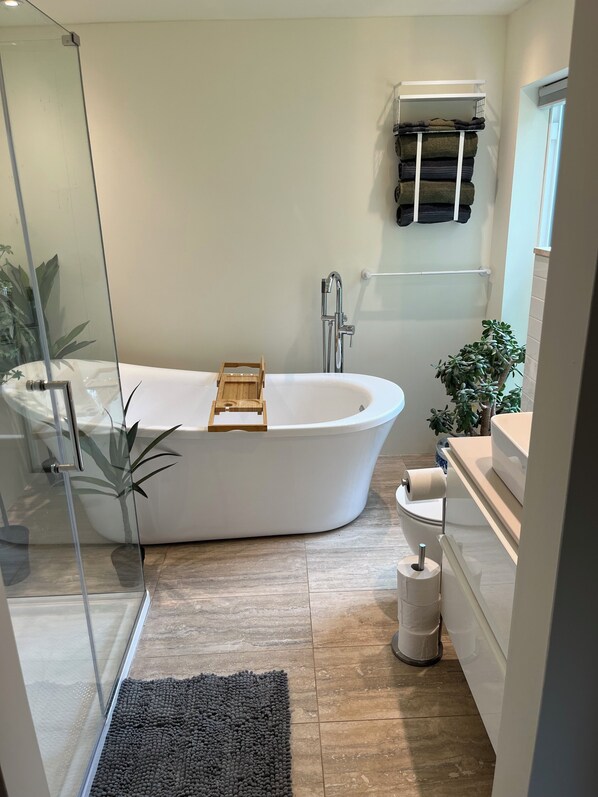 Une salle de bain moderne avec une baignoire sur pieds, une douche en verre, un plateau en bois, des toilettes et un lavabo avec un porte-serviettes.