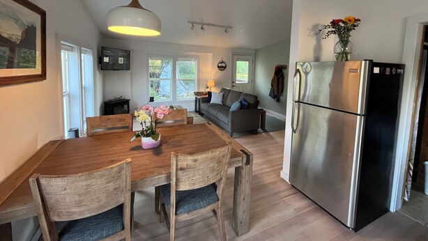 Eine moderne Küche mit Edelstahlkühlschrank, einem Holzespeisetisch mit Stühlen, einer Couch und einer Pendelleuchte.