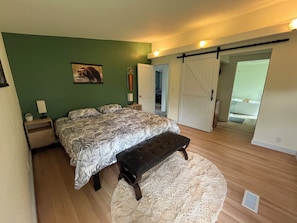 A bedroom with a bed, bench, green walls, and a sliding door.
