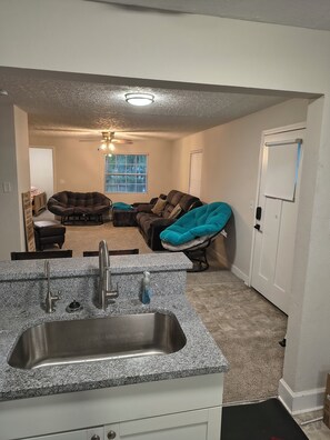 Une cuisine dotée de plans de travail en granit, d’un évier en acier inoxydable et d’une fenêtre avec des stores.