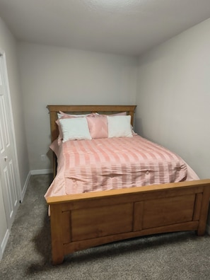A bedroom with a wooden bed frame, a striped bedspread, and two pillows.
