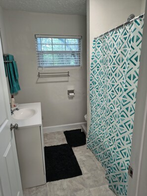 Un baño con ventana, lavamanos, inodoro y cortina de ducha.