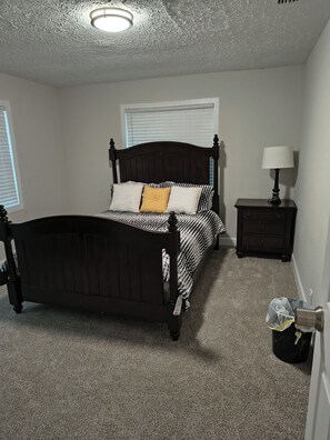 Un dormitorio con cama, mesita de noche, lámpara y bolso en el suelo.