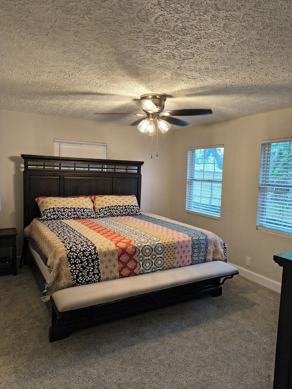 A bedroom with a bed, a ceiling fan, and two windows with blinds.
