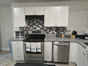 A modern kitchen with white cabinets, a black and white tiled backsplash, stainless steel appliances, and a kitchen island with a sink and utensil holder.