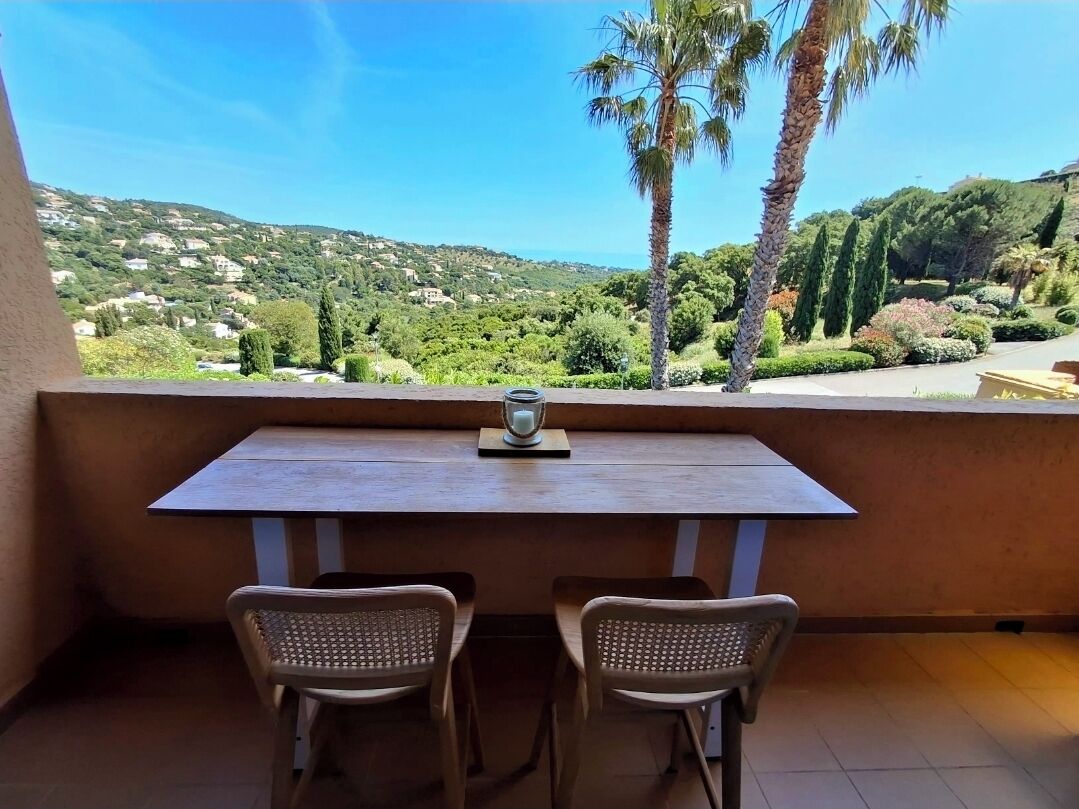 Uma varanda com mesa e duas cadeiras, com vista para uma paisagem deslumbrante com árvores e casas.