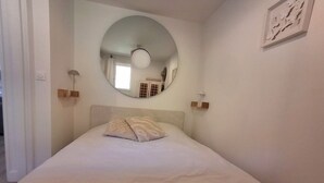 A bedroom with a bed, a round mirror, and a wall-mounted light fixture. - Cozy apartment with a view of the sea and the pool in a private residence. Pets Allowed (Roquebrune-sur-Argens)
