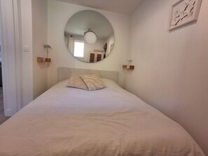 A bedroom with a bed, a round mirror, and a wall-mounted light fixture. - Cozy apartment with a view of the sea and the pool in a private residence. Pets Allowed (Roquebrune-sur-Argens)
