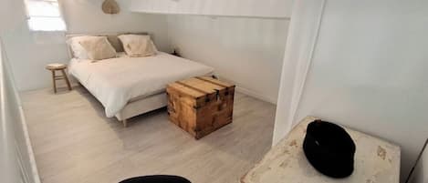 A bedroom with a bed, a wooden chest, a chair, and a white wall.