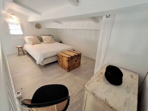Une chambre à coucher avec un lit, une commode en bois, une chaise et un mur blanc.