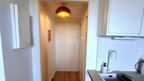 A narrow hallway with wooden flooring leading to a door, a small kitchen area with a sink and cabinets, and a ceiling light fixture. - Cozy apartment with a view of the sea and the pool in a private residence. Pets Allowed (Roquebrune-sur-Argens)