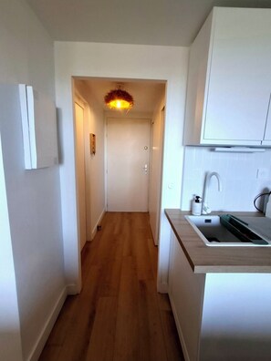 A narrow hallway with wooden flooring leading to a door, a small kitchen area with a sink and cabinets, and a ceiling light fixture. - Cozy apartment with a view of the sea and the pool in a private residence. Pets Allowed (Roquebrune-sur-Argens)