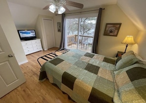 A bedroom with a bed, a television on a dresser, a balcony with a railing, and a ceiling fan.