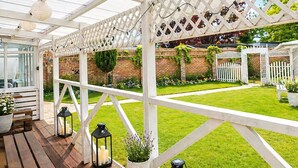 Un patio couvert doté d’une structure en treillis blanc, d’un plancher en bois et de plantes en pot.