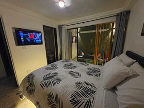 A bedroom with a bed, a television on the wall, and a sliding door leading to an outdoor area with chairs. - Entire lodging at 900 meters from the village station. (Medellín)