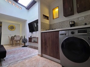 A compact kitchen with a washing machine, a dining area with chairs, a TV, and a decorative wall piece. - Entire lodging at 900 meters from the village station. (Medellín)