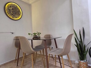 A dining area with a glass table, four woven chairs, a potted plant, and a wall-mounted light fixture. - Entire lodging at 900 meters from the village station. (Medellín)