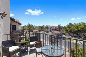 A balcony with wicker furniture, a glass table, and a view of a pool and buildings. - Luxury Resort Condo w/Pool, Spa, Gym & Pickleball 2b/2ba (Scottsdale)