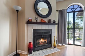 A fireplace with a fire, a round mirror above it, and a window with curtains. - Luxury Resort Condo w/Pool, Spa, Gym & Pickleball 2b/2ba (Scottsdale)