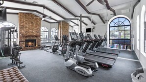 Ett gym med löpband, crosstrainers och en öppen spis i tegel.
