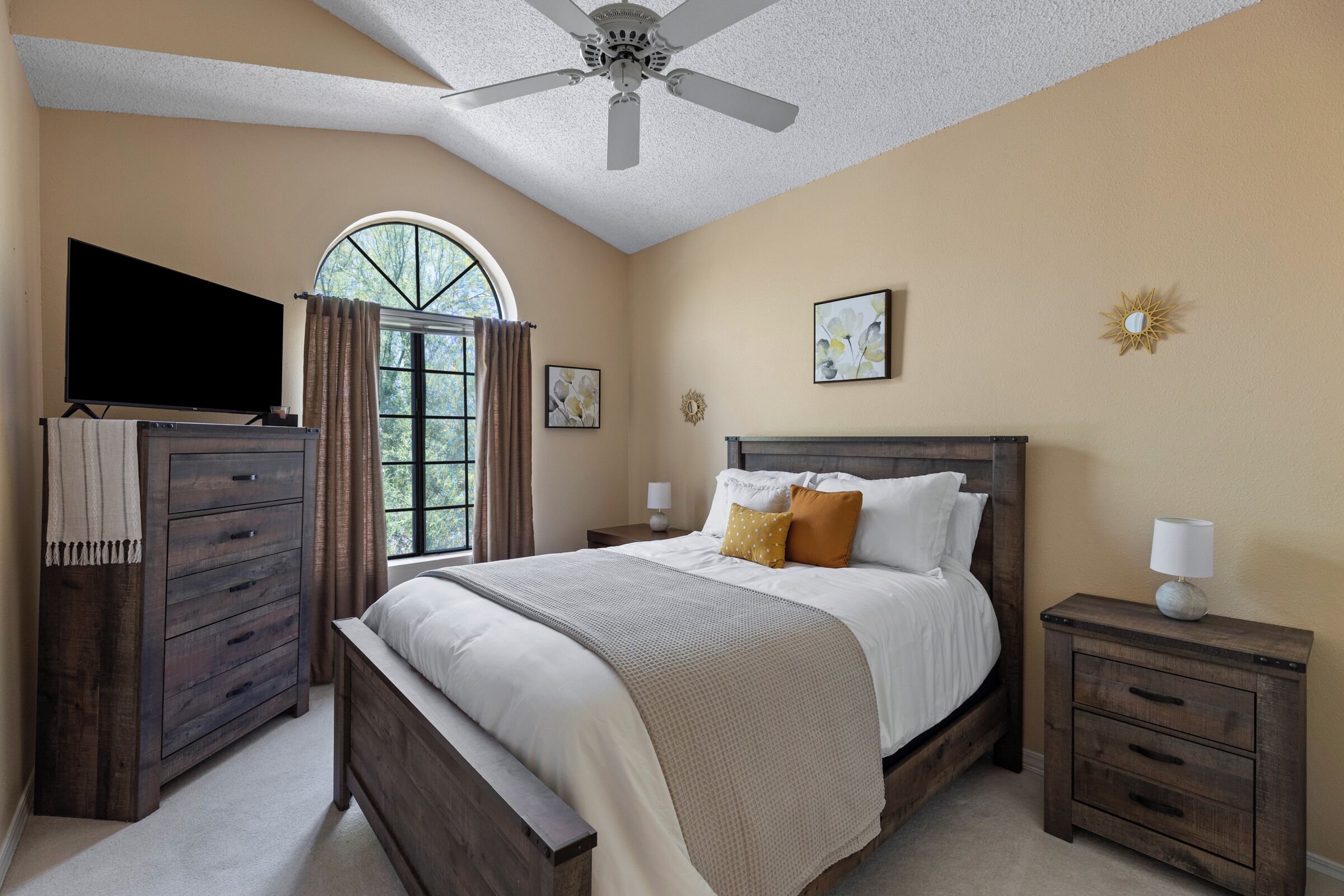 Une chambre à coucher comprenant un lit, une commode, une table de chevet, un téléviseur et un ventilateur de plafond.