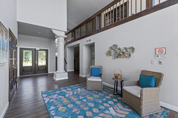 A spacious foyer with a high ceiling, dark wooden flooring, and two wicker chairs with blue cushions. - Luxury Resort Condo w/Pool, Spa, Gym & Pickleball 2b/2ba (Scottsdale)