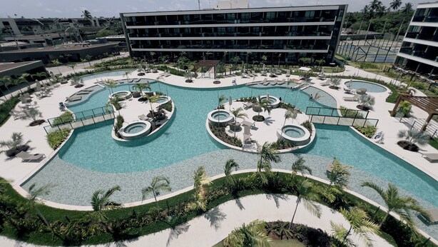 Un resort con piscina centrale, zone relax e un edificio moderno sullo sfondo.