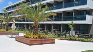 Un edificio moderno con diversi balconi, posti a sedere all'aperto e una zona verde con palme.