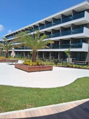 A modern building with multiple balconies, outdoor seating, and a landscaped area with palm trees. - Fully equipped studio apartment in the Beach Class Verano building on Muro Alto beach. (Ipojuca)