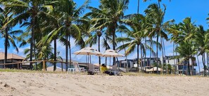A beach with palm trees, beach chairs, and umbrellas. - Fully equipped studio apartment in the Beach Class Verano building on Muro Alto beach. (Ipojuca)