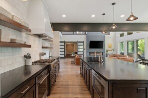 Une cuisine moderne dotée d’un grand îlot central, de meubles en bois et de luminaires suspendus.
