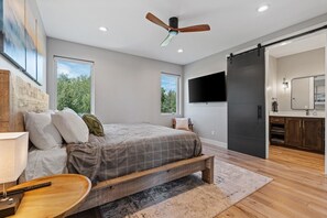 A modern bedroom with a bed, a ceiling fan, a TV, and a sliding door leading to a bathroom.