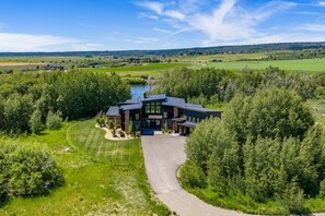 Une maison moderne dotée d’une grande allée, entourée d’une végétation luxuriante et bordée d’un lac.