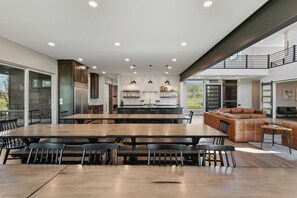 A spacious dining area with a large wooden table and benches, a kitchen with modern appliances, and a view of the outdoors.