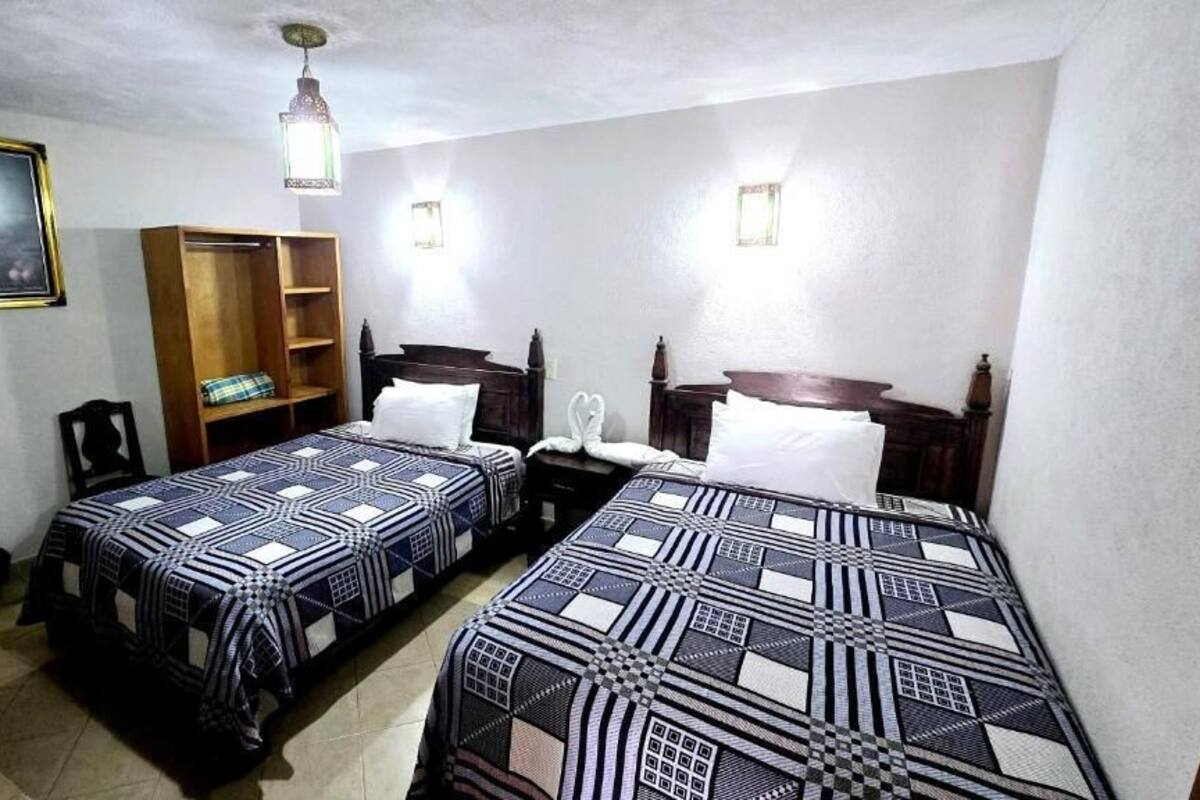 Una habitación con dos camas, un armario de madera, un ventilador, un cuadro enmarcado y un ventilador de techo.