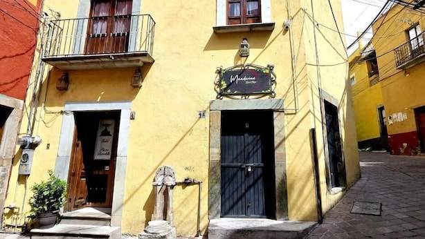 A yellow building with a black door, a balcony, and a sign that reads 'Mandelia.' - Hotel Plaza Baratillo (Guanajuato)