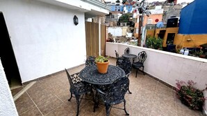 A small outdoor patio with a round table and chairs, a potted plant, and a view of a densely packed urban neighborhood. - Hotel Plaza Baratillo (Guanajuato)