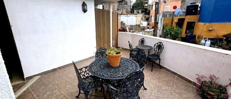 A small outdoor patio with a round table and chairs, a potted plant, and a view of a densely packed urban neighborhood.