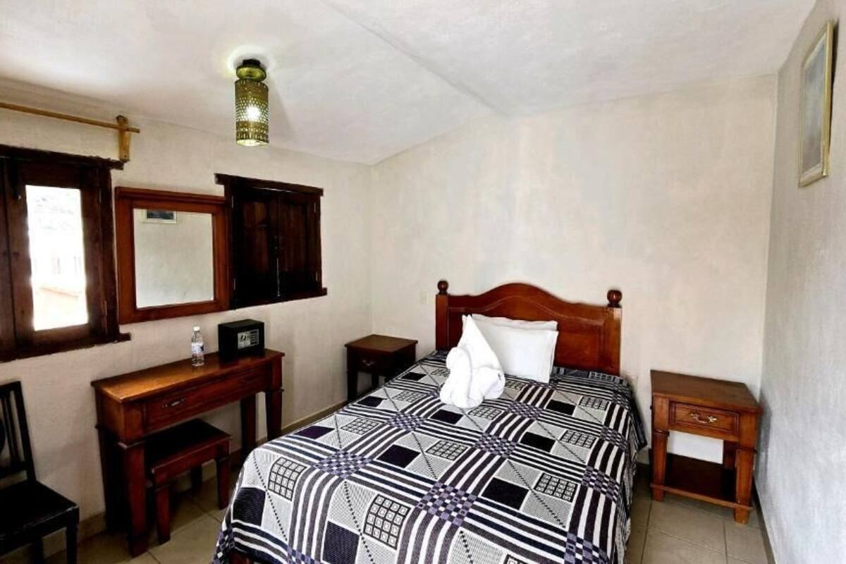 Un dormitorio con cama, escritorio, silla, mesita de noche, lámpara y ventana.