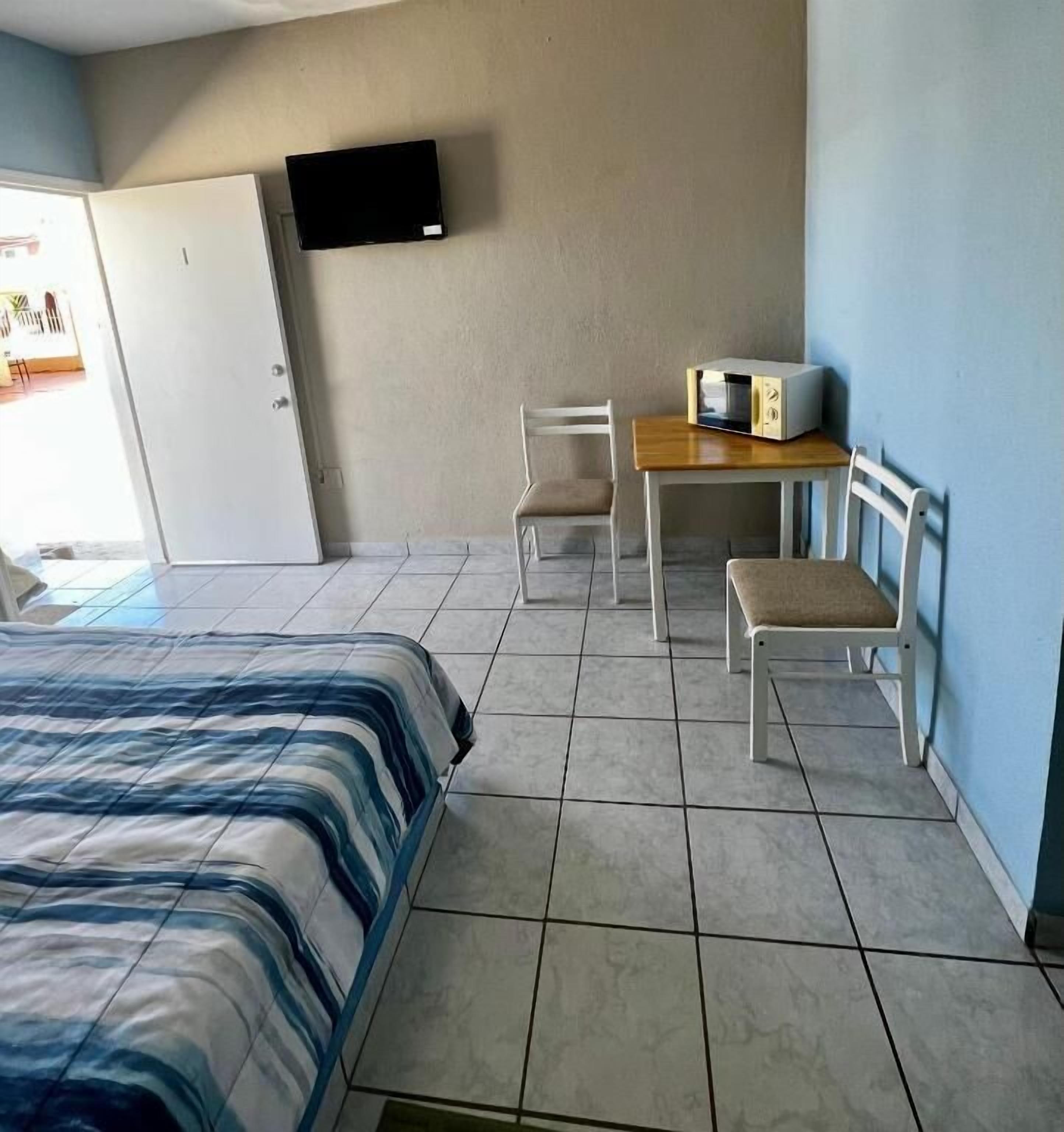Una habitación con una cama, un escritorio con una silla, un televisor en la pared y una puerta.
