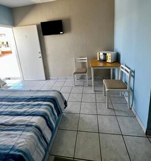Una habitación con una cama, un escritorio con una silla, un televisor en la pared y una puerta.