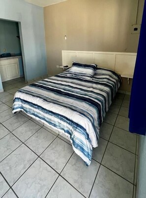 Un dormitorio con cama, cabecera y suelo de baldosas.